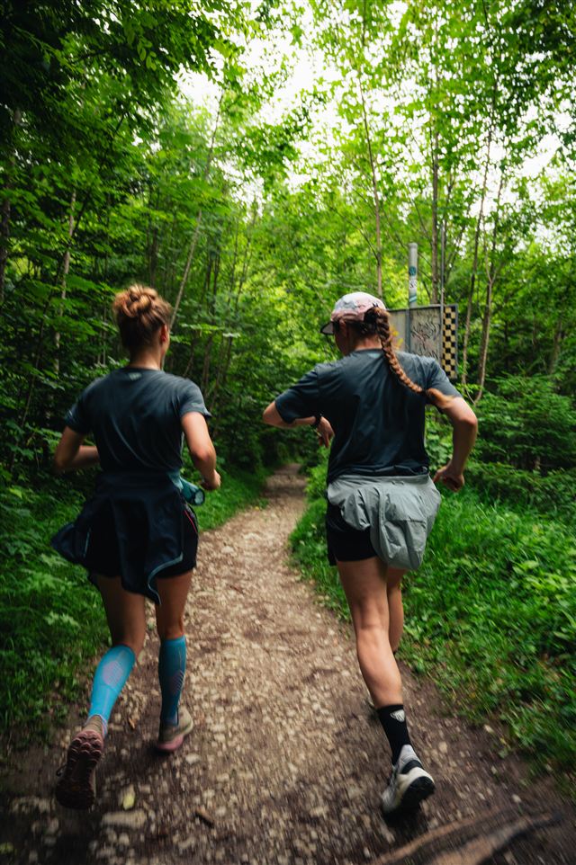 Two trail runners following a narrow path through the forest